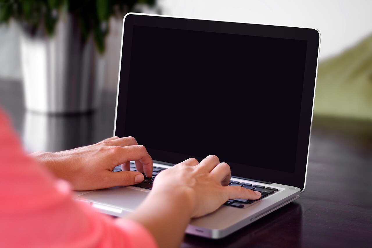 Mains sur le clavier d’un ordinateur portable posé sur un bureau
